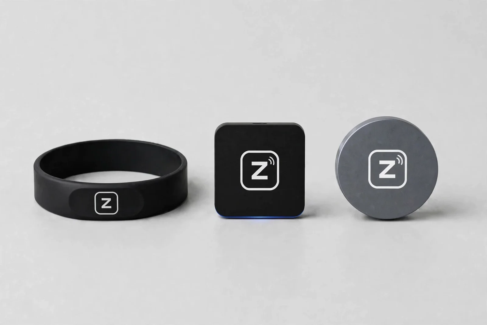 Zovo wristband, wall tag, and counter puck side by side, each with the white Zovo emblem centered